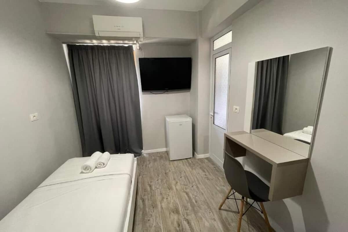A hotel room with a bed, a desk, a television, a mini-fridge, and a window with curtains.