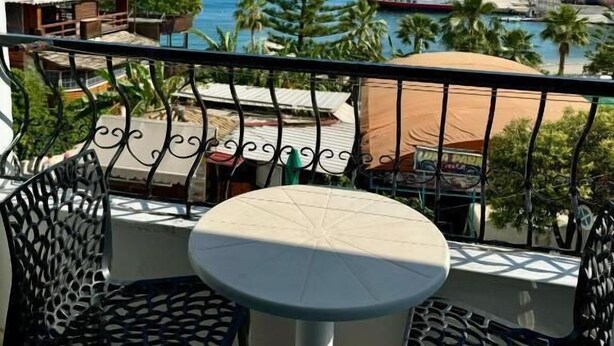 Varanda com mesa e cadeiras, vista para uma marina com barcos e para a costa.