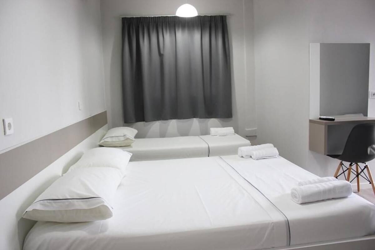 A hotel room with two single beds, a desk, a chair, and a large window with curtains.
