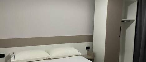 A modern hotel room with a large bed, a wardrobe, and a ceiling light.
