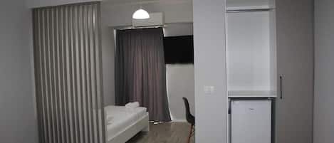 Quarto de hotel pequeno com uma cama, uma escrivaninha, uma cadeira, um guarda-roupa e um mini-frigorífico.