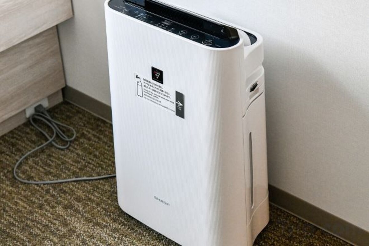 A white portable air purifier with a control panel and a power cord plugged in.