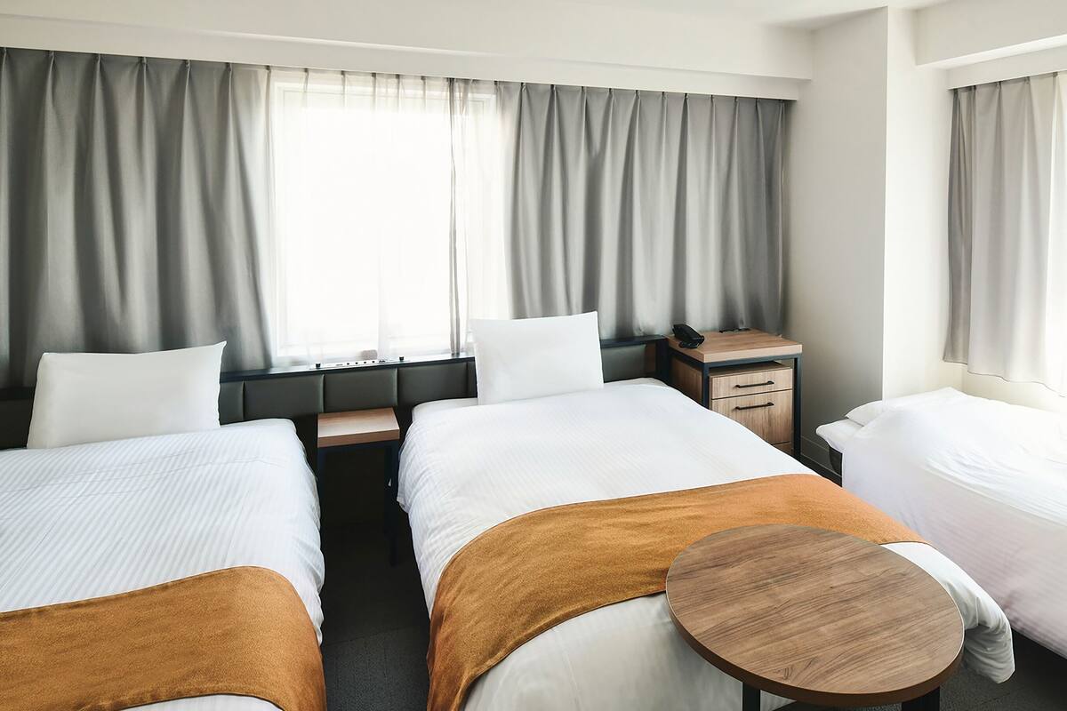 Een hotelkamer met twee bedden, een klein houten tafeltje, een bureau met telefoon en een raam met gordijnen.