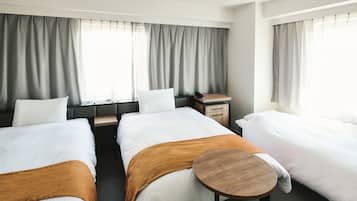 A hotel room with two beds, a small wooden table, a desk with a phone, and a window with curtains.