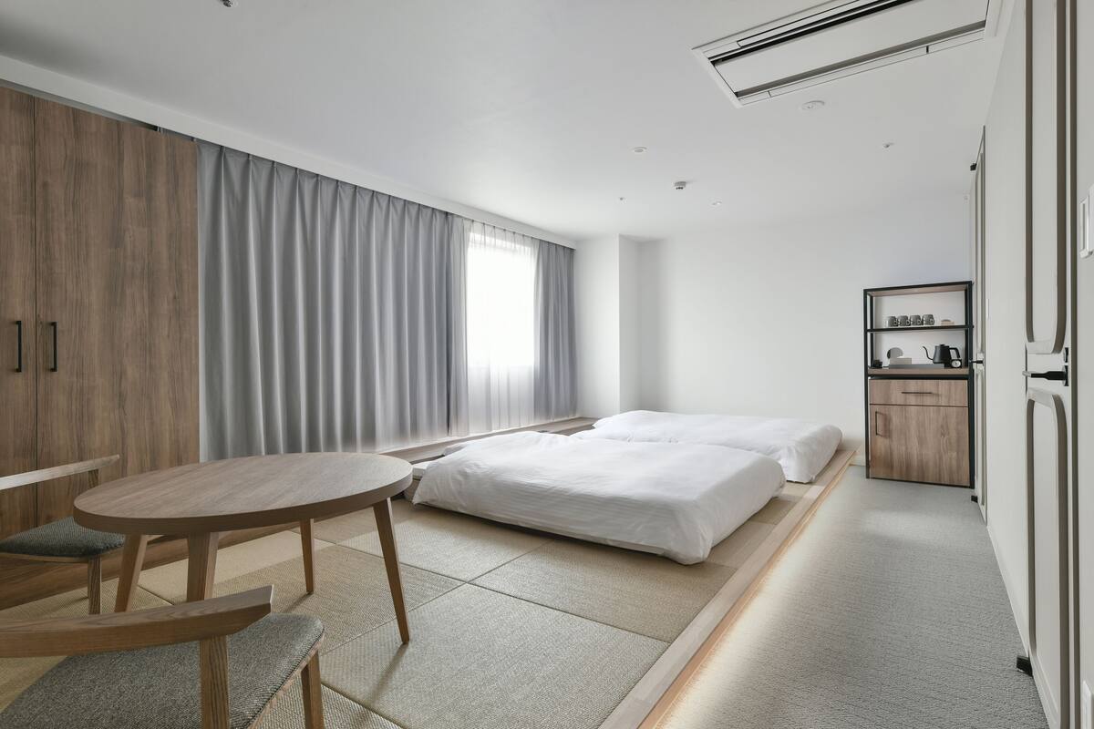 Een moderne hotelkamer met een bed, een klein tafeltje, een stoel, een kledingkast en een nachtkastje met een lamp.