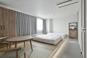 Ein modernes Hotelzimmer mit einem Bett, einem kleinen Tisch, einem Sessel, einem Kleiderschrank und einem Nachttisch mit Lampe.