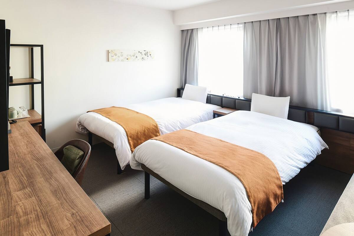 Een hotelkamer met twee bedden, een bureau en een raam met gordijnen.