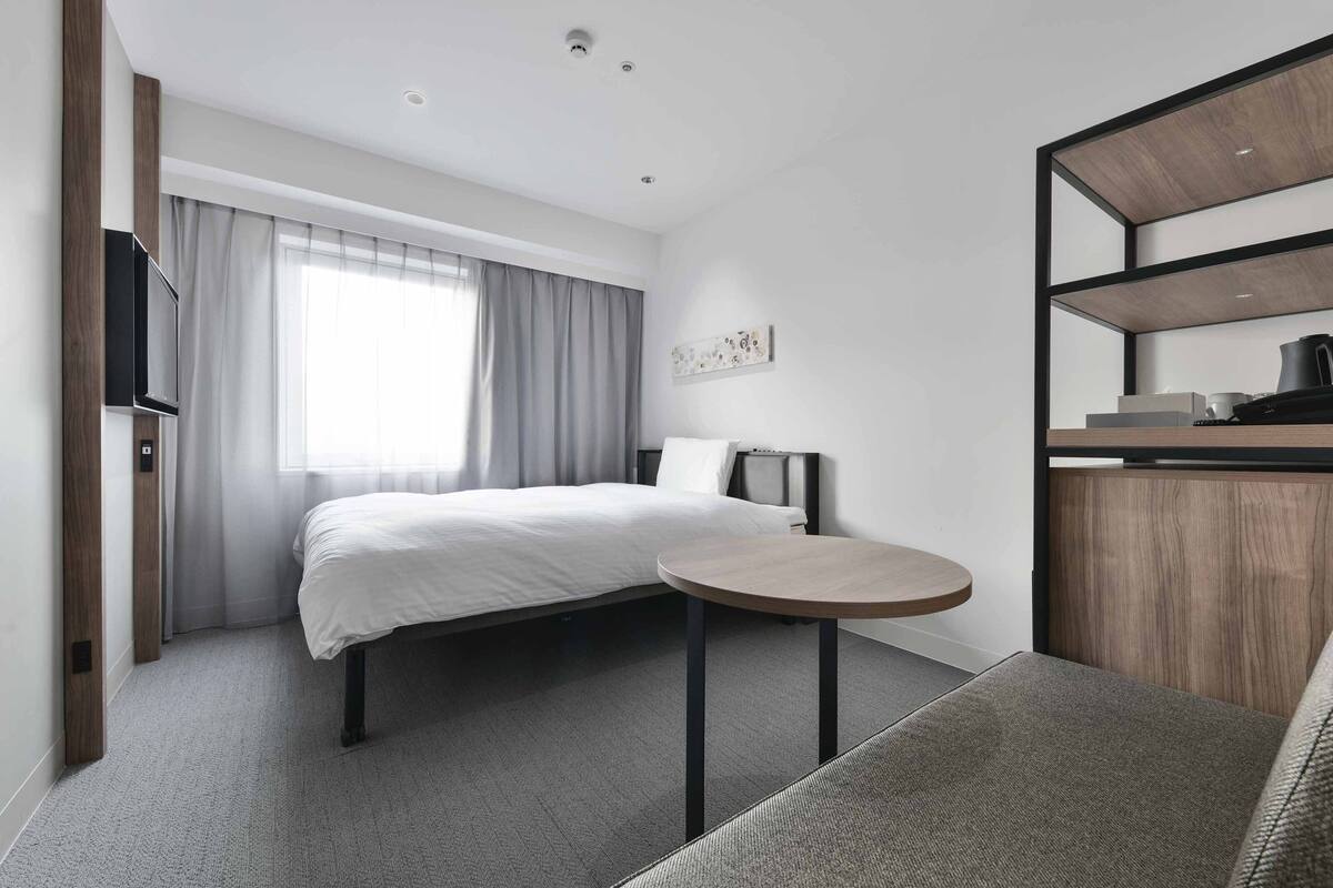 Een moderne hotelkamer met een bed, een ronde tafel, een televisie en een inbouwkast met spullen.