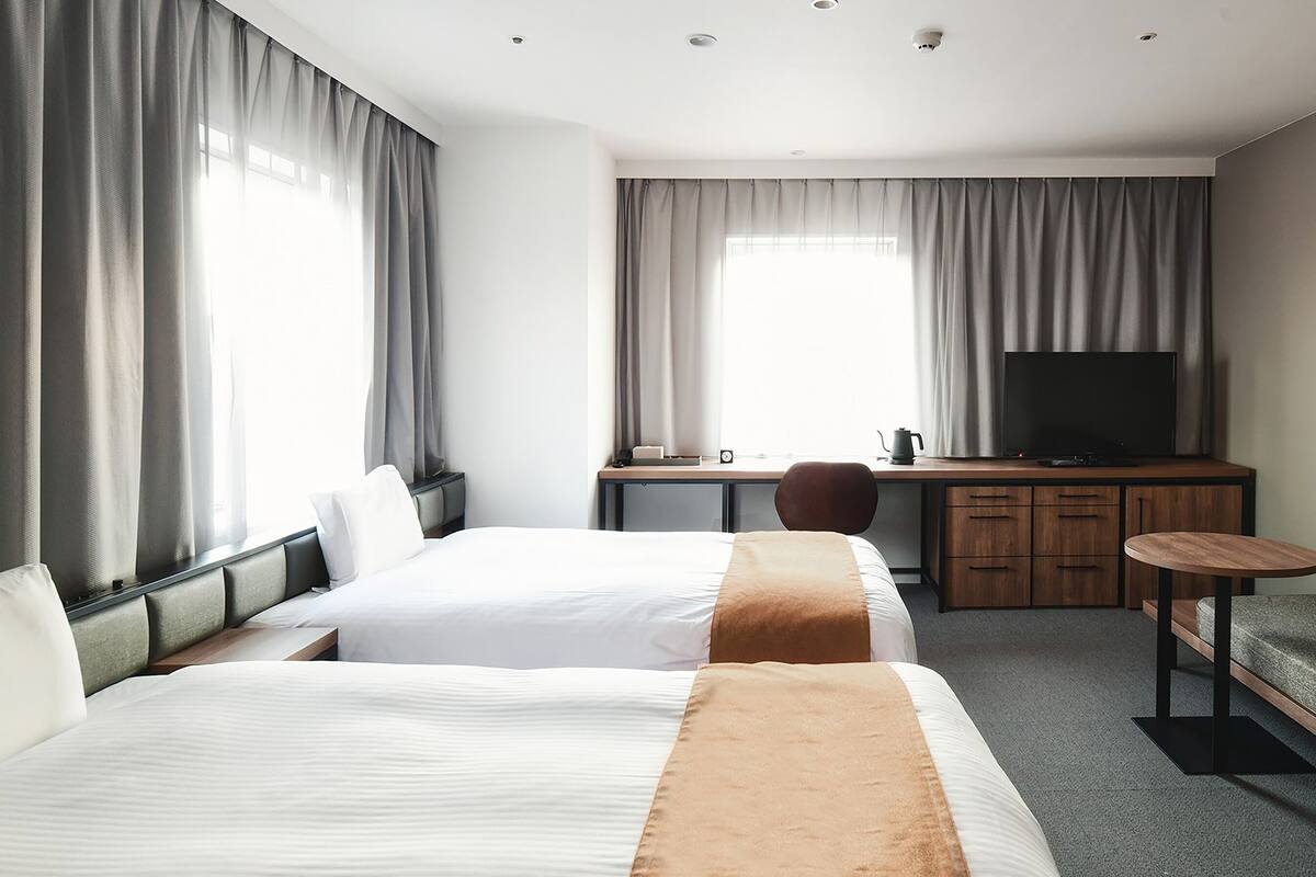 Een hotelkamer met twee bedden, een bureau met een televisie, een stoel en een klein tafeltje.