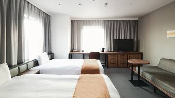 Habitación de hotel con dos camas, un escritorio con televisor, una silla y una mesita.