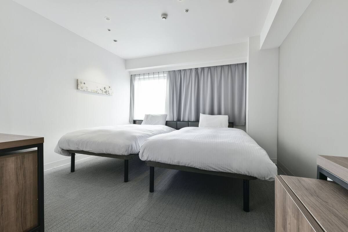 Een moderne hotelkamer met twee enkele bedden, een bureau en een groot raam met gordijnen.