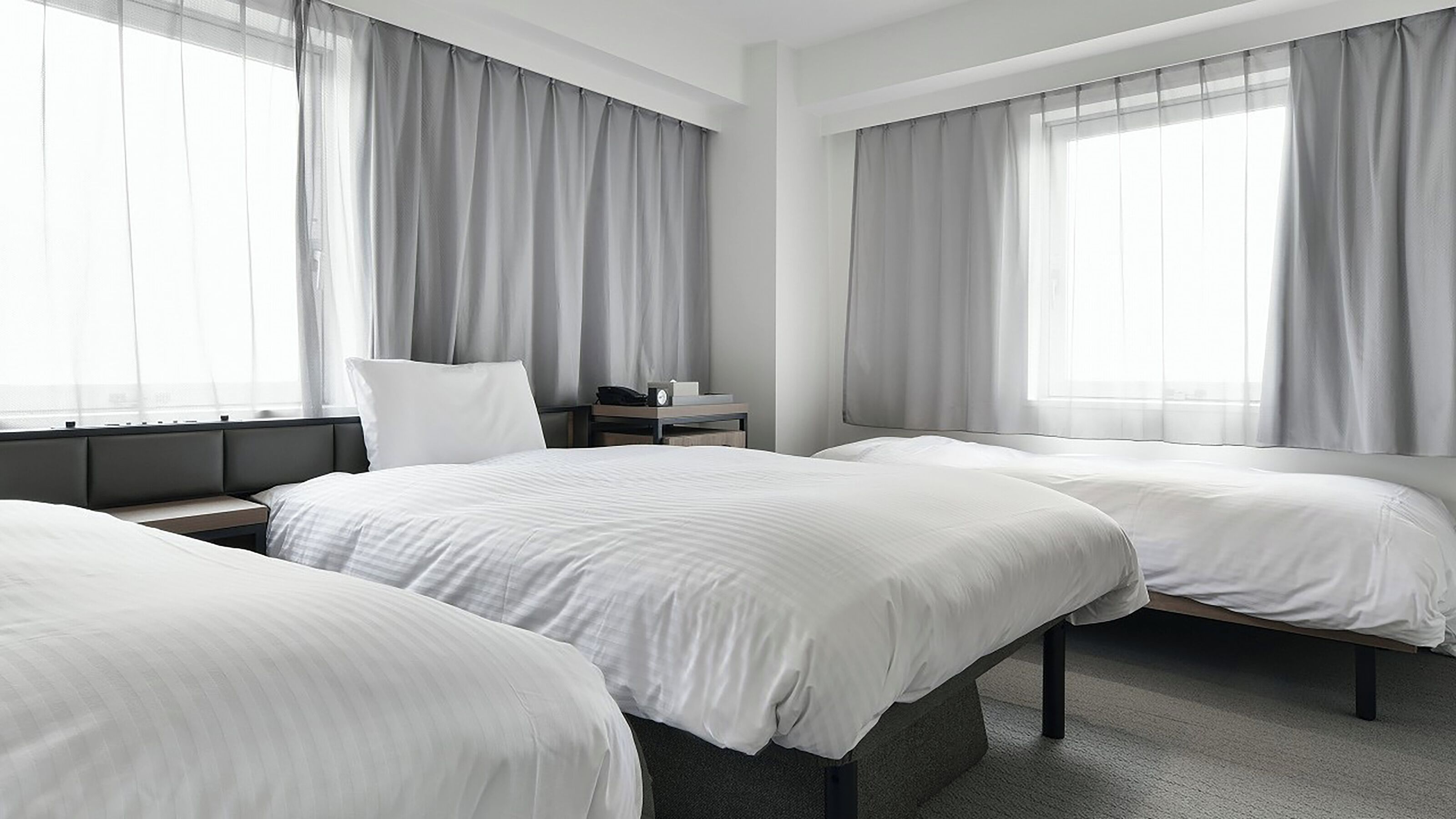 Habitación de hotel con dos camas, una mesita de noche y una ventana con cortinas.
