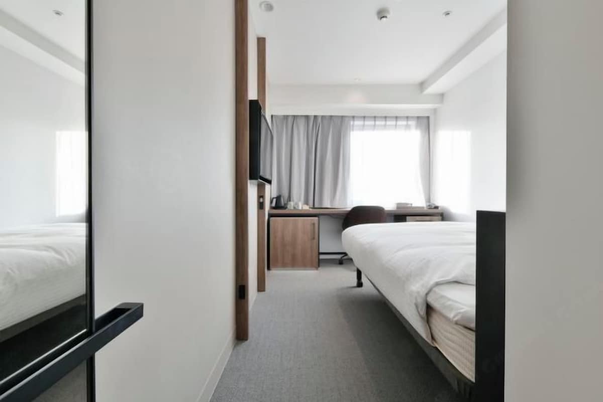 Una habitación de hotel moderna con una cama grande, un escritorio con silla, un televisor y una ventana con cortinas.
