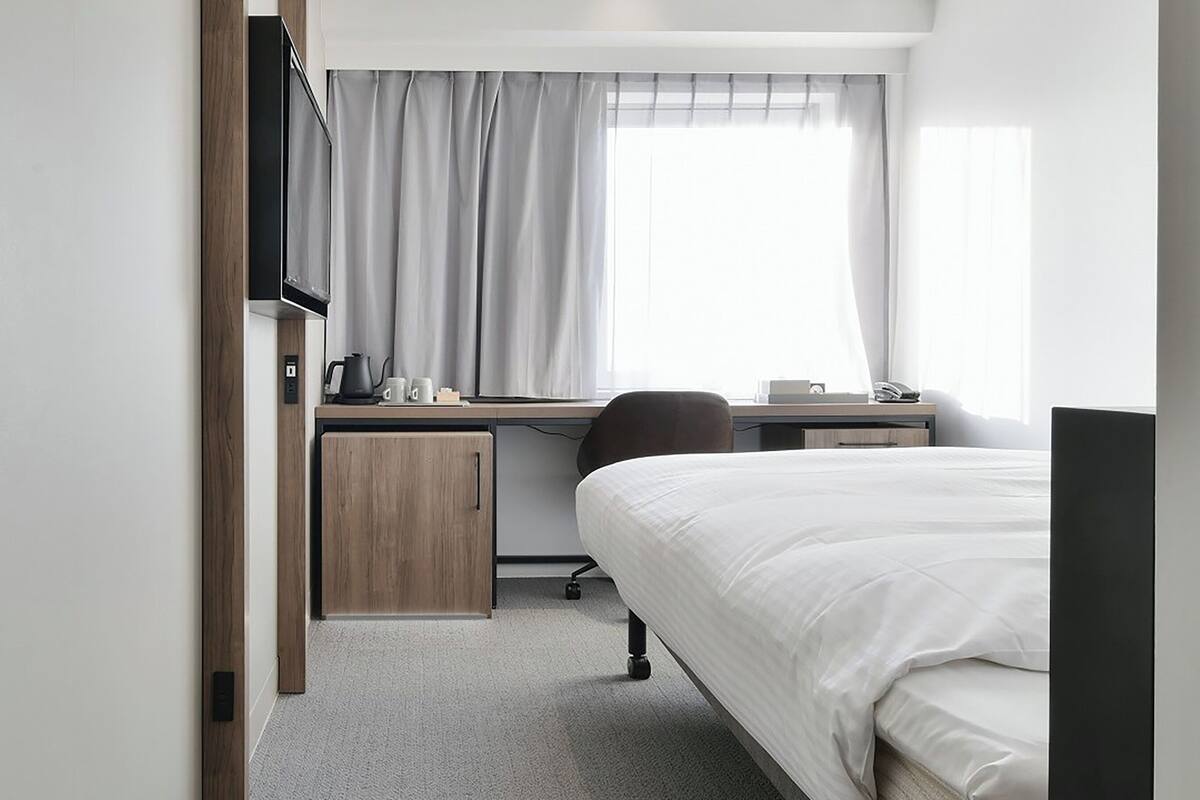 Een hotelkamer met een bed, een bureau met stoel, een televisie en een raam met gordijnen.