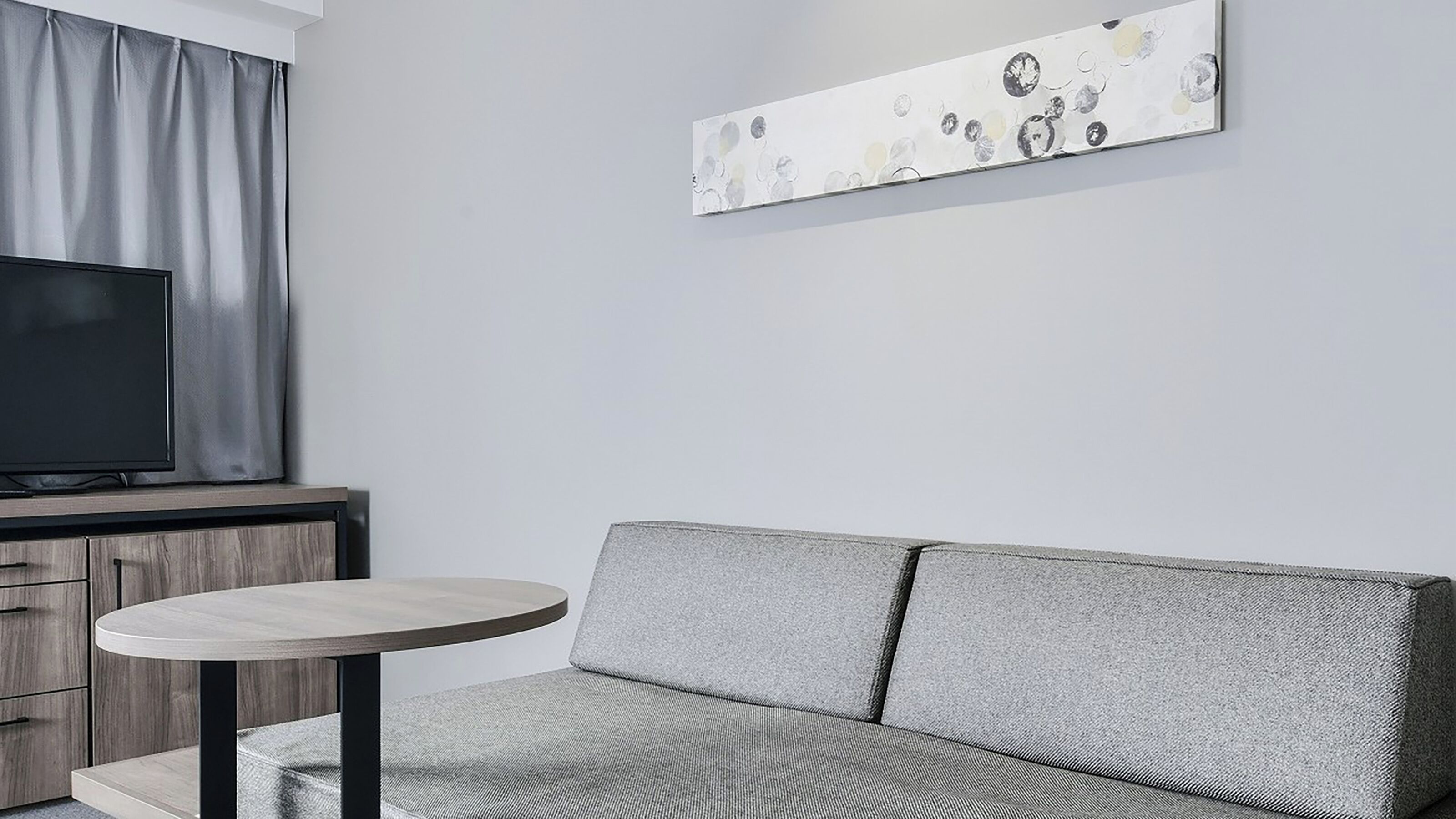 A modern living room with a grey sofa, a round wooden table, and a flat-screen TV on a wooden cabinet.
