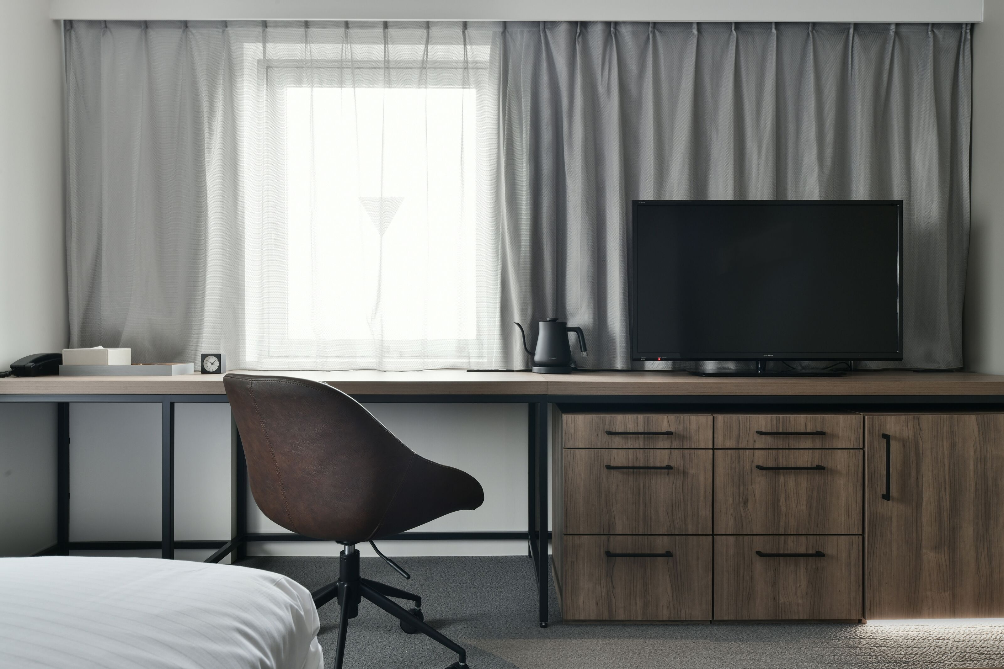 Une chambre d’hôtel avec un lit, un bureau avec une télévision, une chaise et une fenêtre avec des rideaux.