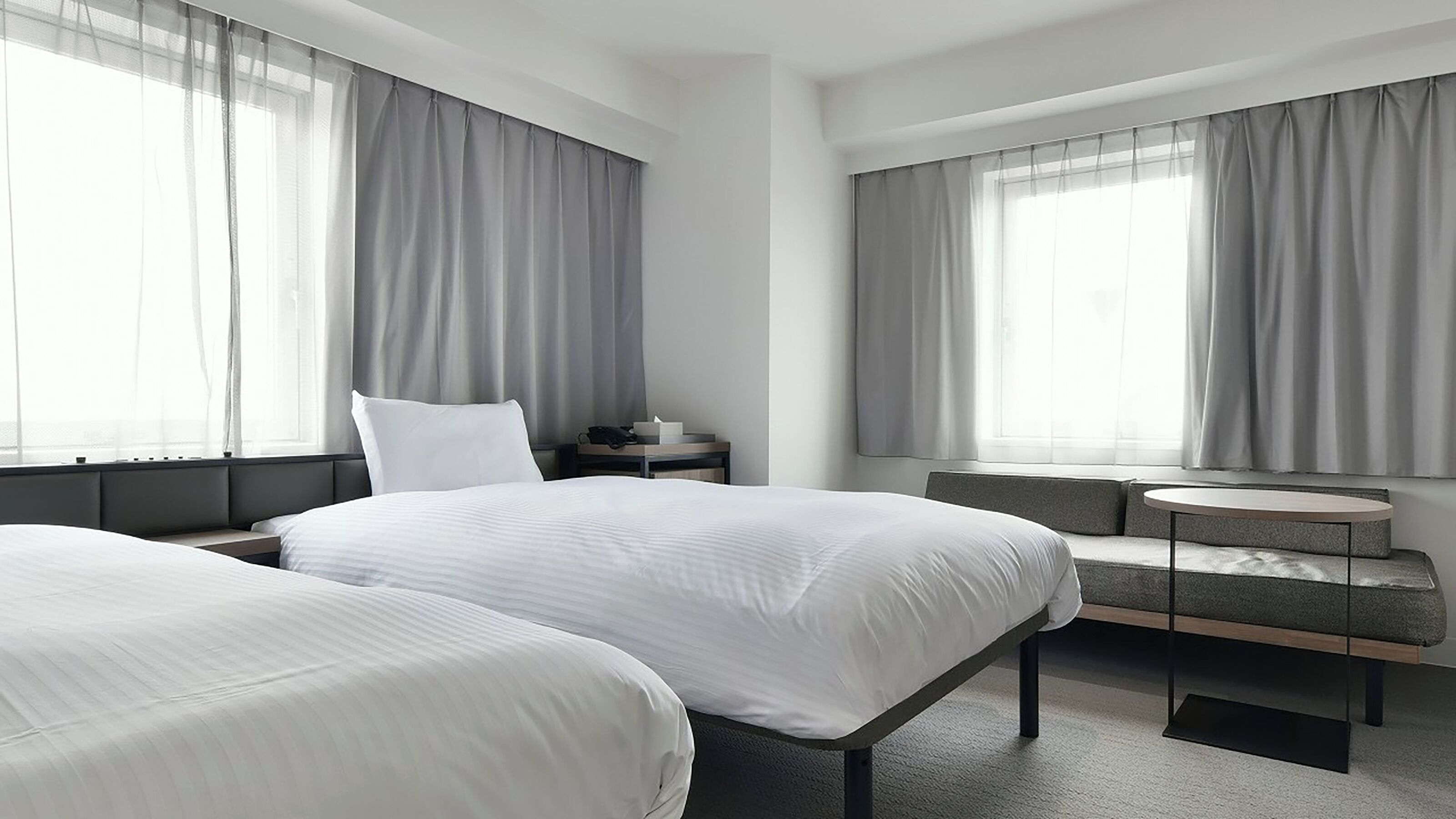 A modern hotel room with two beds, a small table, and a bench.