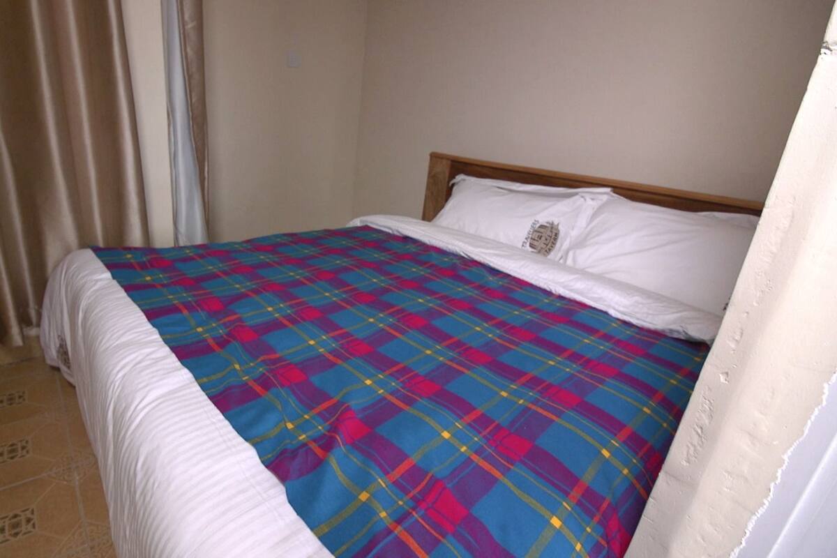 A bedroom with a bed, a window with curtains, and a tiled floor.