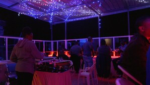 An outdoor dining area with tables and chairs, under a covered structure with string lights. - Travellers Tavern (Nkubu)