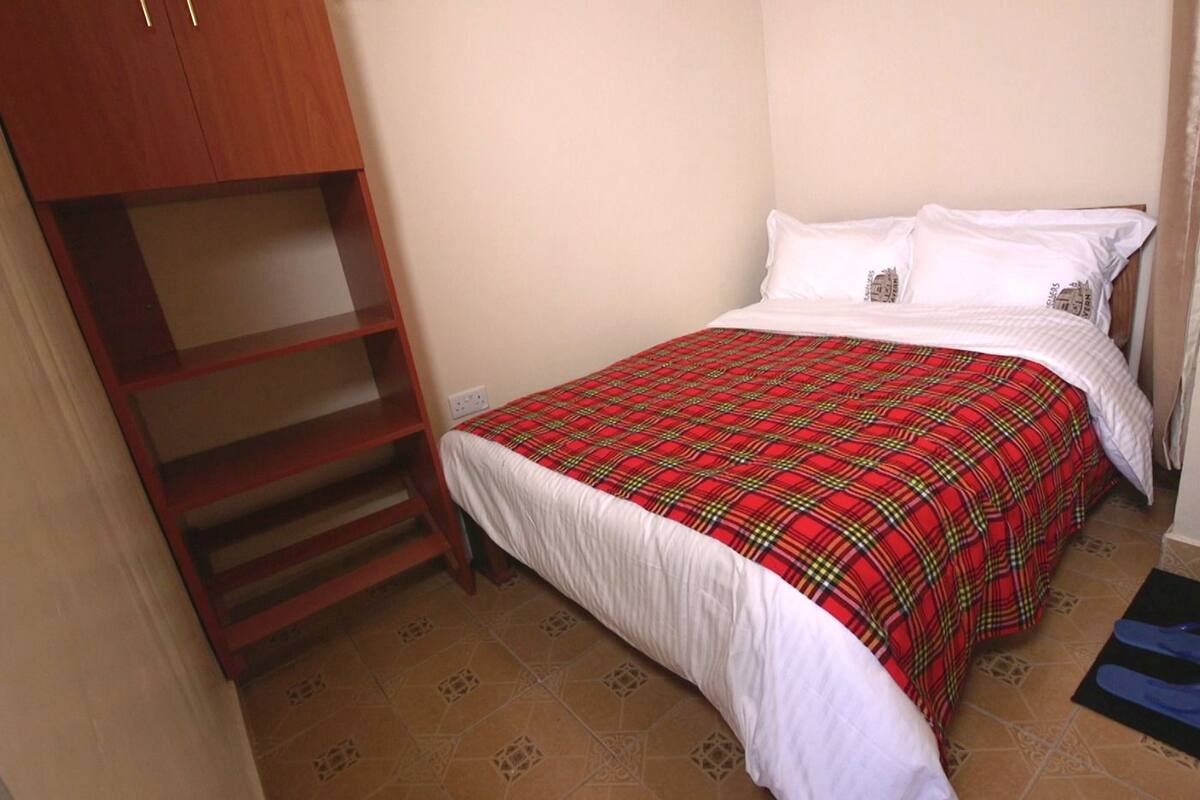 A bedroom with a bed, a wooden wardrobe, and a red plaid bedspread.