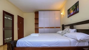 A bedroom with a wooden bed, white bedding, a wardrobe, and a painting on the wall. - Nairobi Luxury Suites (Nairobi)