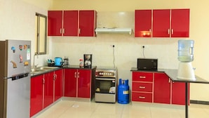 A compact kitchen with red cabinets, a refrigerator, a stove, and a microwave. - Nairobi Luxury Suites (Nairobi)