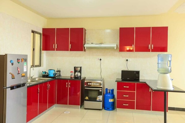 Une cuisine de taille réduite avec des meubles de rangement rouges, un réfrigérateur, une cuisinière et un four à micro-ondes.