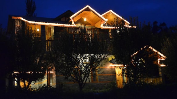 A house with a sloped roof, wooden exterior, and illuminated exterior lights. - Gezellig Inn - Kanyal Villas (Manali)