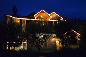 A house with a sloped roof, wooden exterior, and illuminated exterior lights. - Gezellig Inn - Kanyal Villas (Manali)
