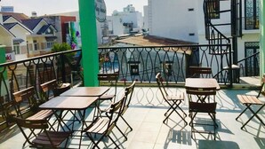 Une terrasse sur le toit, avec des tables et des chaises, un pilier végétalisé et une vue sur les bâtiments environnants.