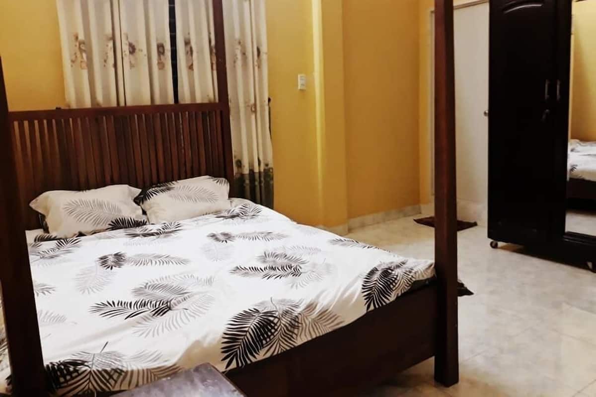 Un lit à baldaquin avec une couvre-lit ornée de motifs de feuilles, une tête de lit en bois et un rideau à motifs floraux.