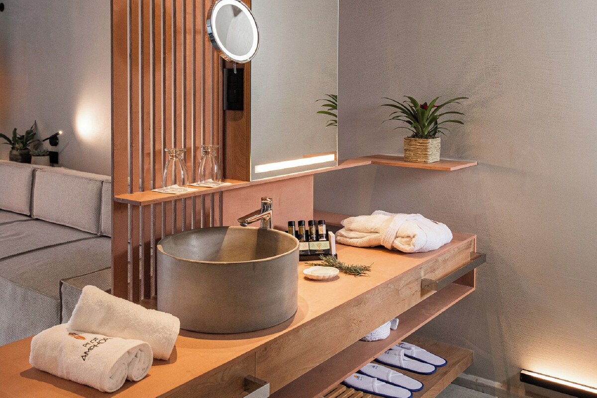 A modern bathroom with a large round sink, wooden shelves, a mirror, and a potted plant.