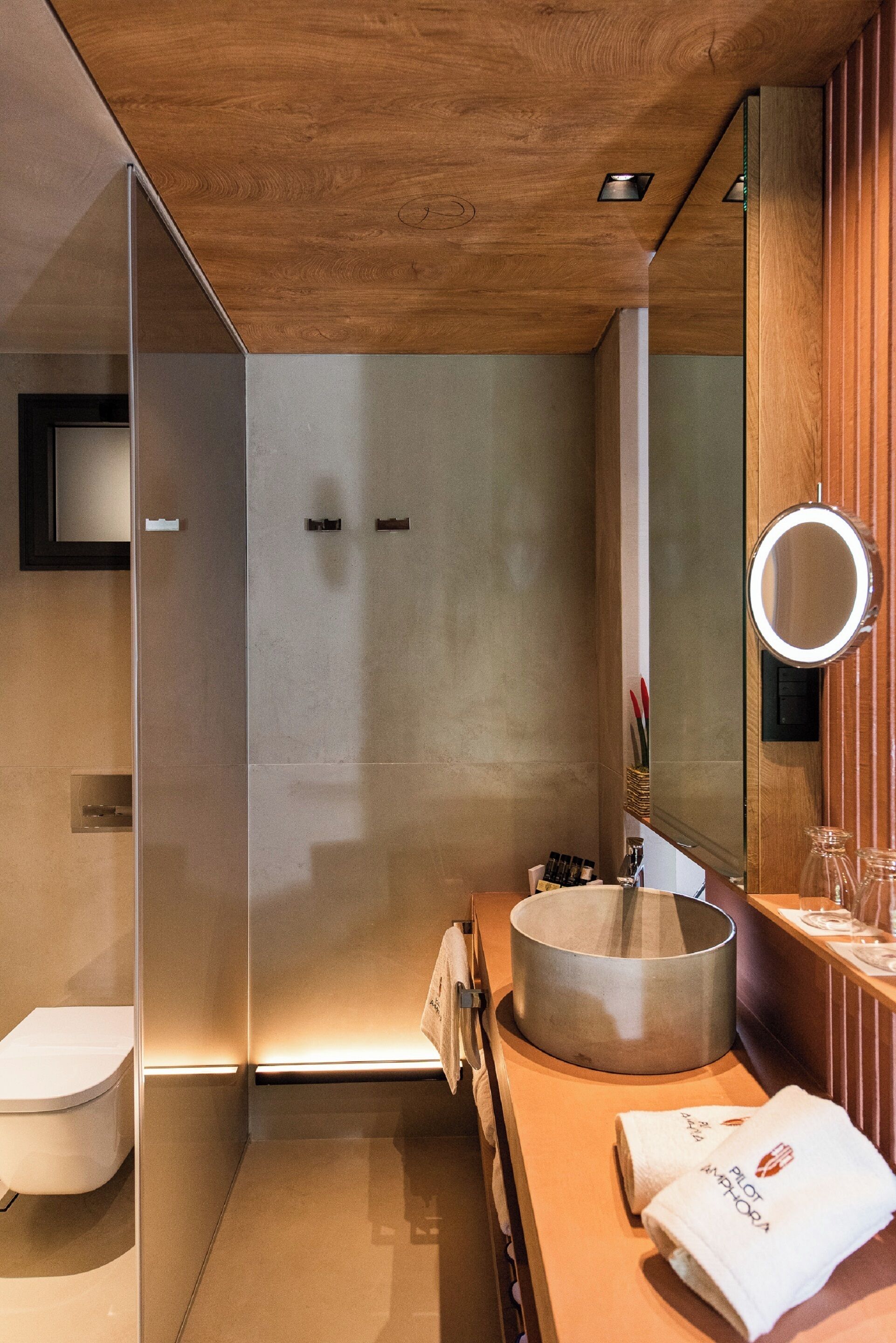 A modern bathroom with a glass shower enclosure, a round sink, and a wooden vanity.