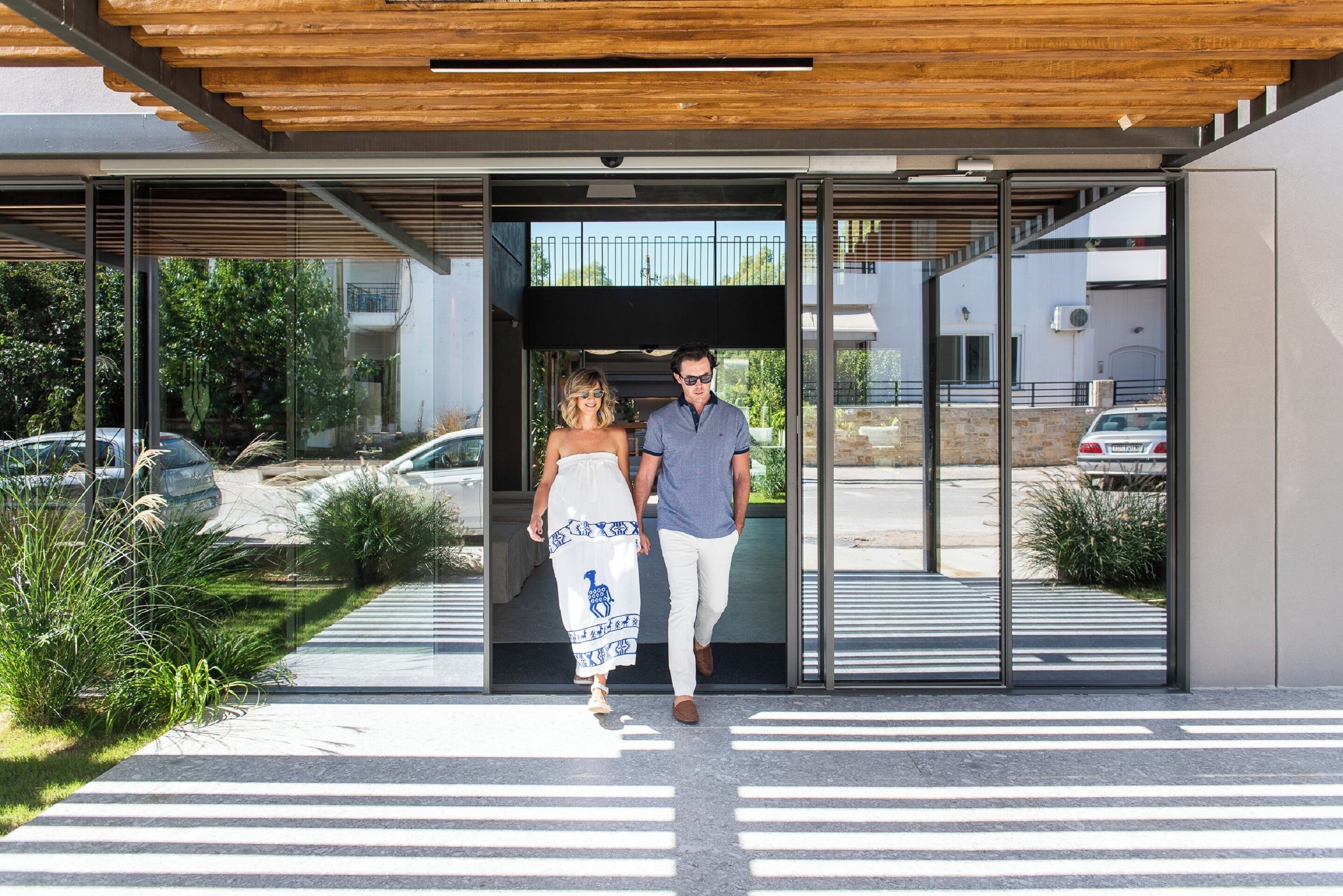 A modern building entrance with glass doors, a wooden ceiling, and a paved walkway leading to the entrance.