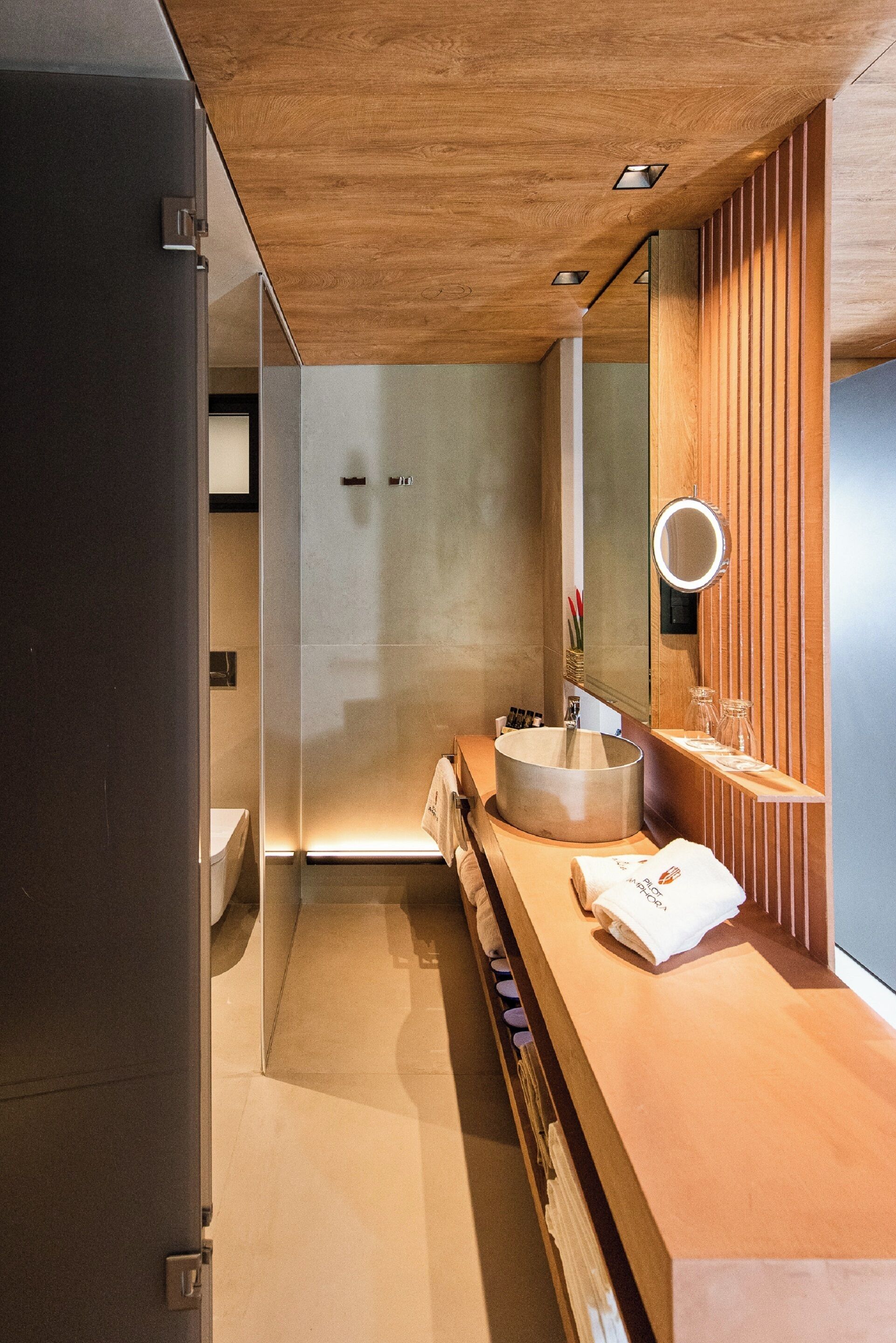 A modern bathroom with a wooden vanity, a round mirror, and a built-in sink.