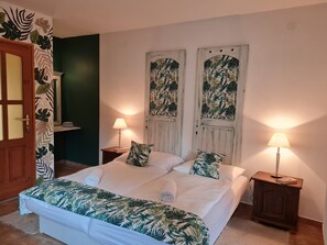 Une chambre à coucher comprenant un lit, deux tables de chevet, une porte et un mur orné d’un motif de feuilles tropicales.