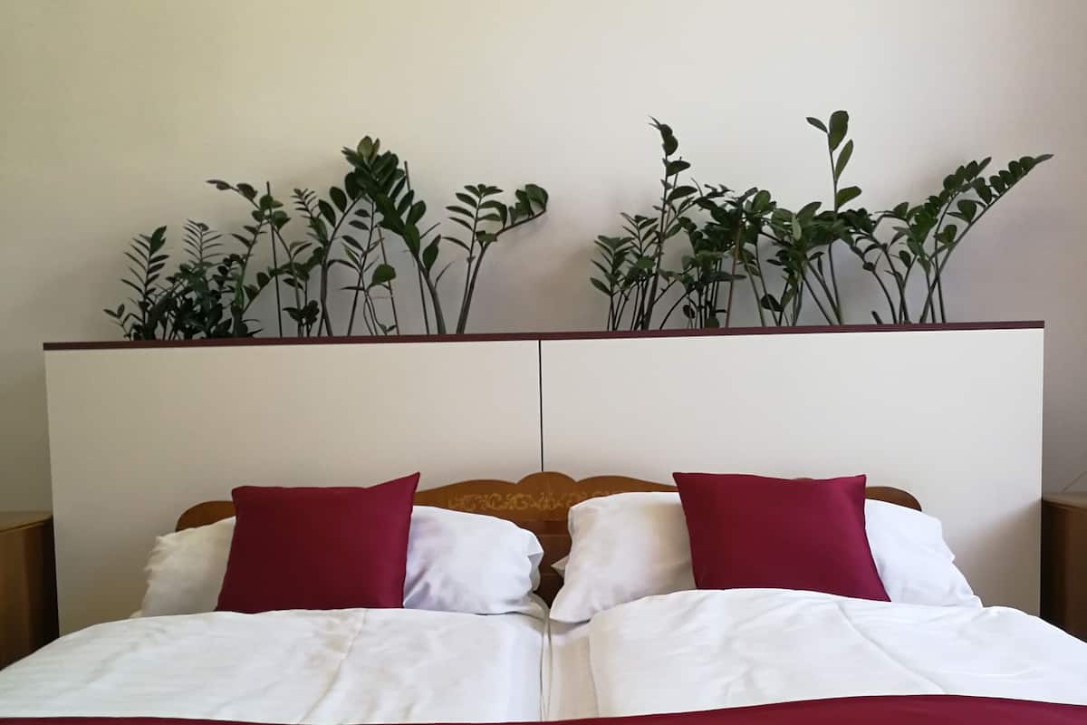 A double bed with white and red bedding, a wooden headboard with a decorative design, and a plant arrangement on the wall behind the bed.