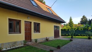 Un bâtiment jaune avec un toit en tuiles, deux portes en bois et un petit jardin agrémenté de plantes en pot.