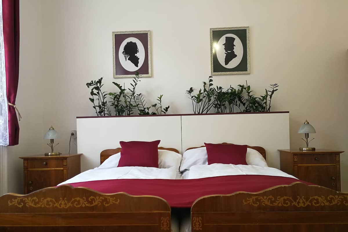 A double bed with a red and white bedspread, two nightstands with lamps, and two framed portraits on the wall.