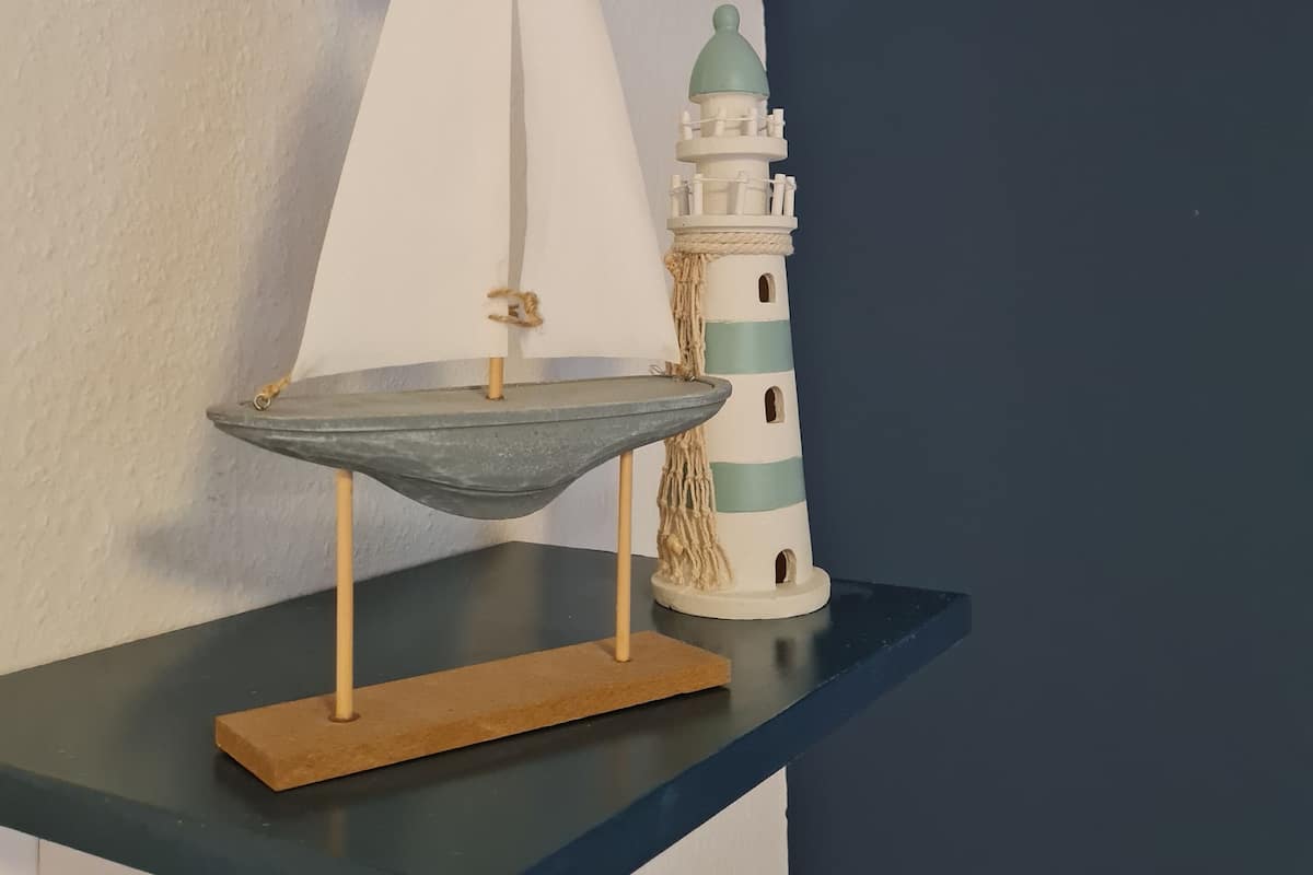 A model sailboat and a lighthouse on a shelf.