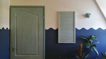 A room with a wooden floor, a green door, a blue wall with a wave pattern, a potted plant, and a wall-mounted air conditioning unit.