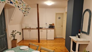 Un coin repas avec une table dressée pour quatre personnes, une cuisine en arrière-plan et un miroir au mur.