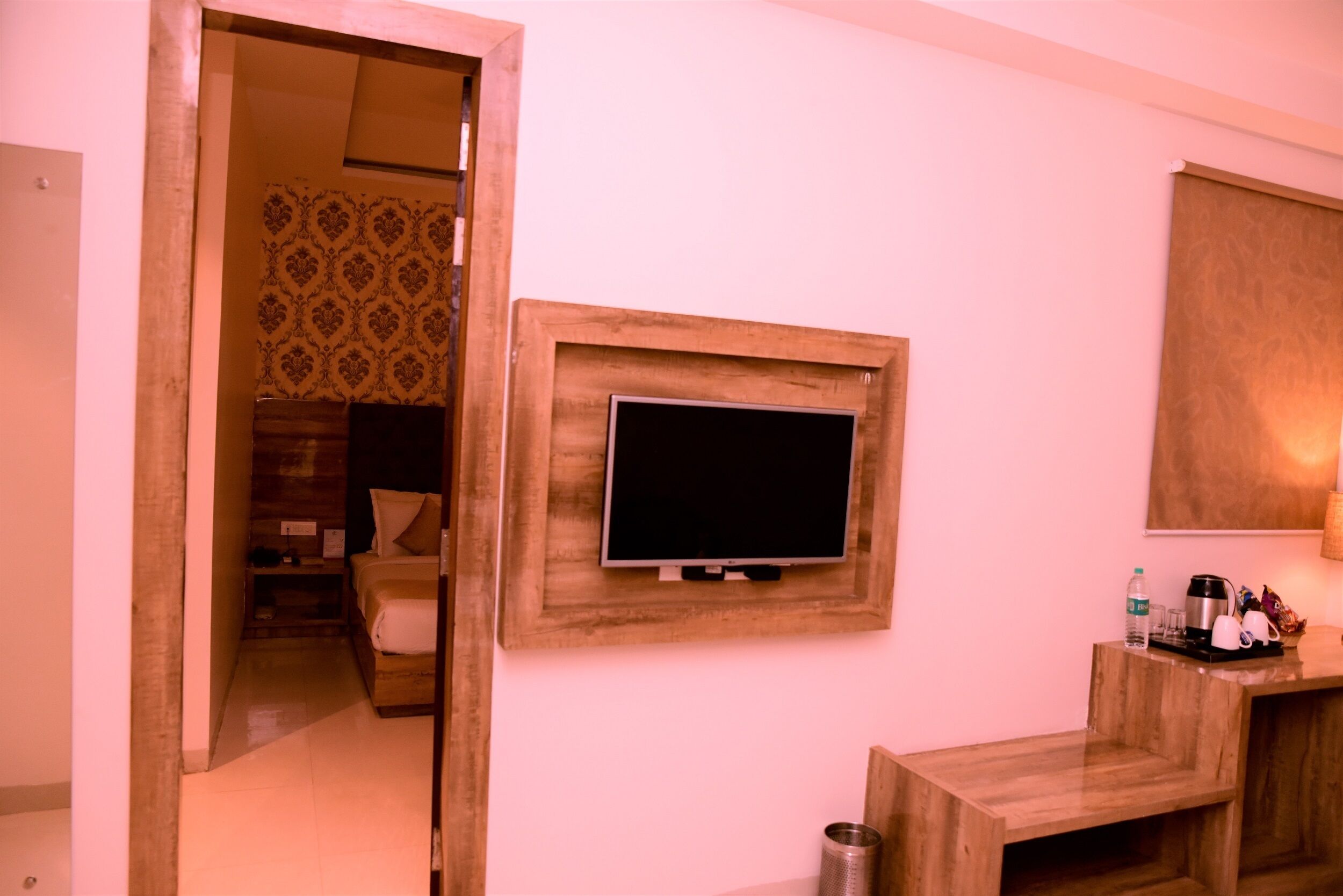 Ein Hotelzimmer mit Fernseher an einer Holzwand, einem Bett mit gemustertem Kopfteil und einer kleinen Sitzecke mit Tisch und Stühlen.