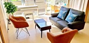 A modern living room with a black leather sofa, two orange armchairs, a glass coffee table, and a potted plant.