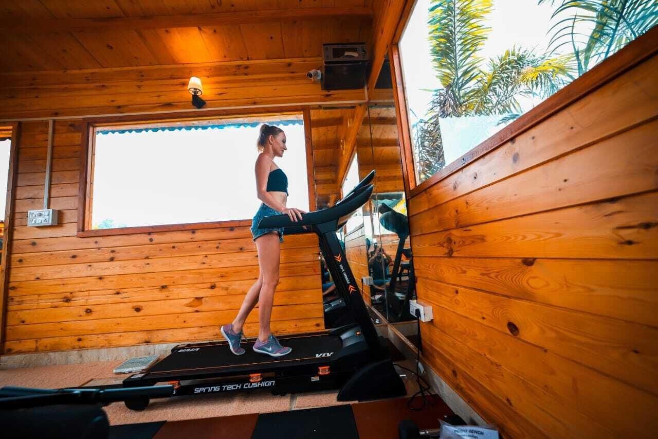 A person using a treadmill in a wooden cabin with large windows and a view of palm trees.