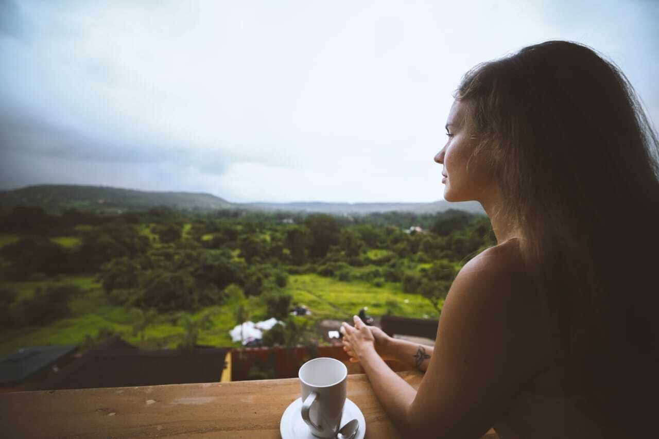 Une personne est assise à une table, une tasse à portée de main, et elle a devant elle un paysage verdoyant.