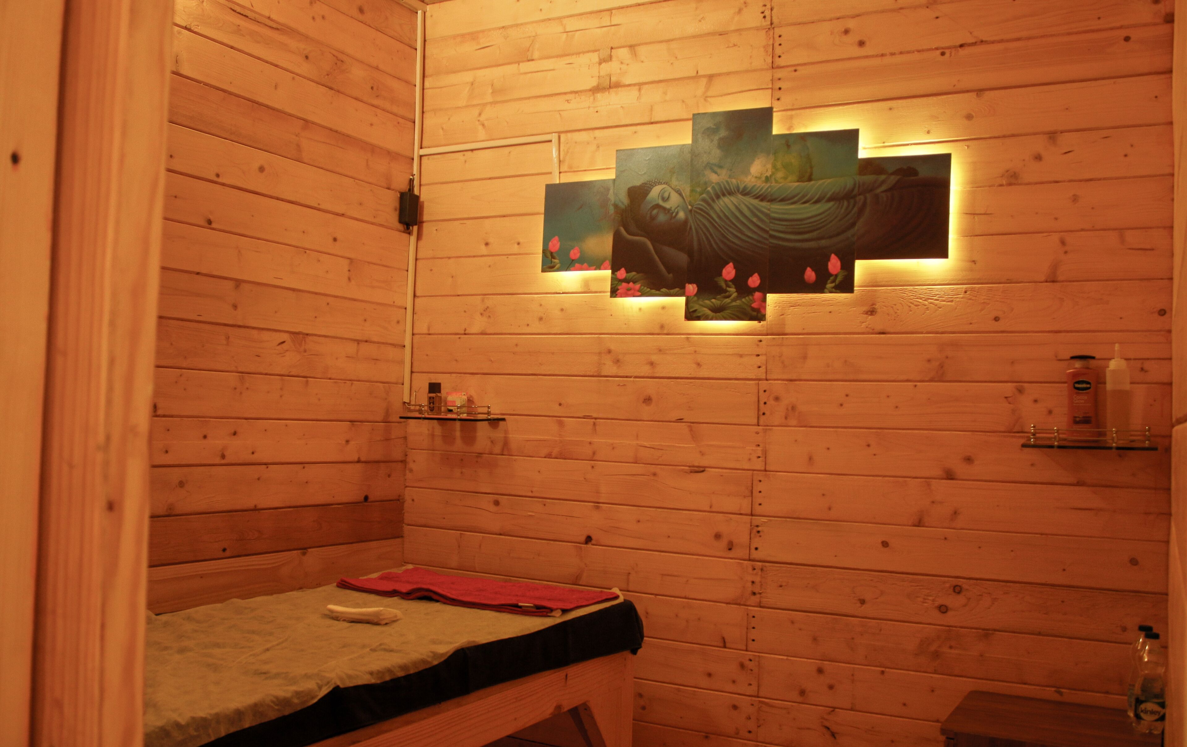 A wooden room with a massage table, a shelf with toiletries, and a wall-mounted artwork.