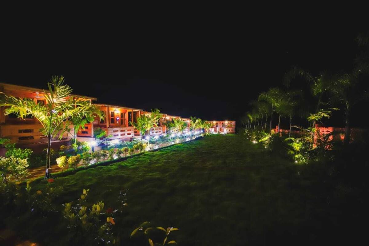 A hotel with a well-lit exterior, a pool area, and a variety of tropical plants.