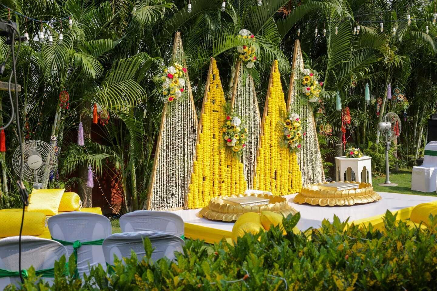 A tropical outdoor setting with a stage decorated with flowers and greenery, surrounded by palm trees.