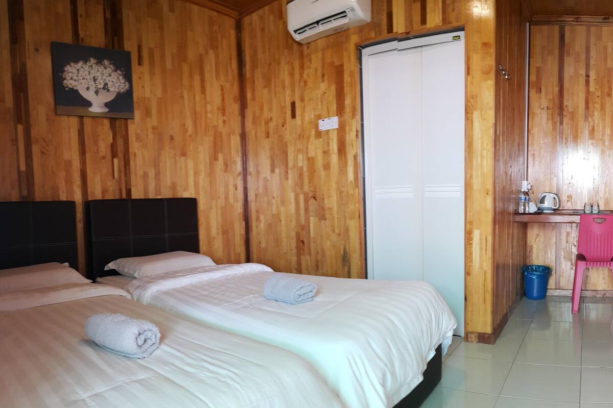 A hotel room with wooden panel walls, a bed with white linens, a painting of flowers, a white door, and a small kitchenette area.